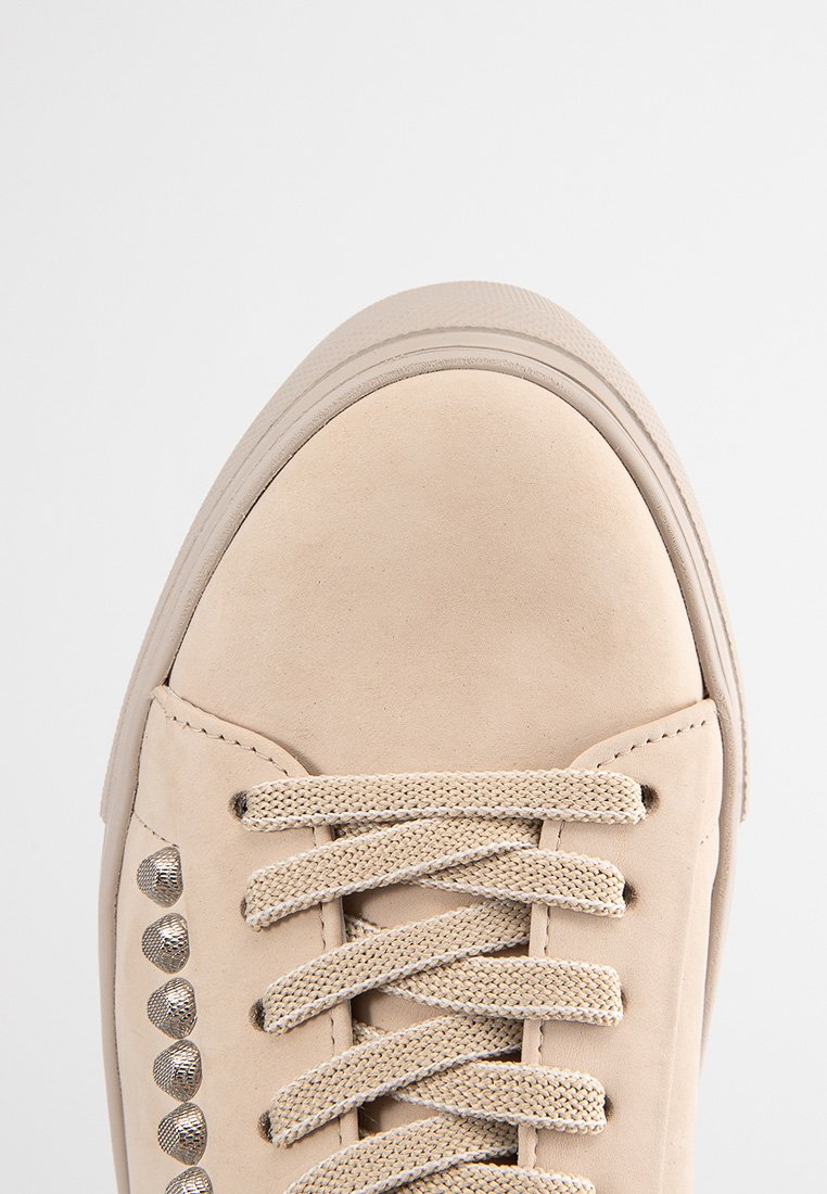 Beige Wildlederschuh mit runder Zehenpartie, flacher Gummisohle und dekorativen Metallnieten entlang der Seite. Verfügt über flache beigefarbene Schnürsenkel.