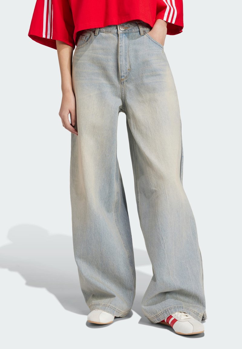 Light blue wide-leg jeans made of denim, featuring a high waist and subtle fading. Paired with a red cropped top and white sneakers.