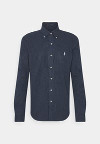 Mörkblå skjorta med knappar och vita prickar, långa ärmar och spetsig krage. Har en liten logotyp på bröstet och knappstängning.