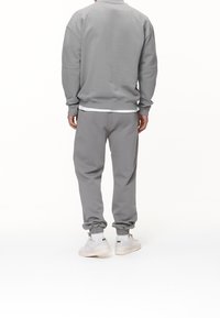 Felpa grigia e pantaloni jogger in morbido misto cotone, con polsini a costine e vestibilità rilassata. Sneakers chiare completano l'outfit.