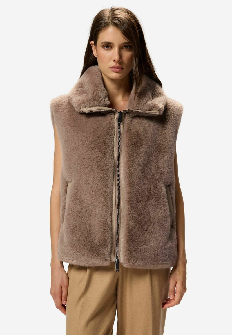 Prsni brezrokavnik iz umetnega krzna v mehki rjavi barvi, z visokim ovratnikom, sprednjim zadrgo in brez rokavov. Gladke teksture z bočnimi žepi.