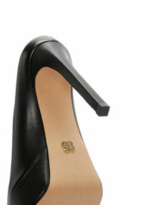 Zapato de tacón alto de cuero negro con punta cuadrada, textura suave y tacón delgado. Presenta un emblema dorado en la plantilla.