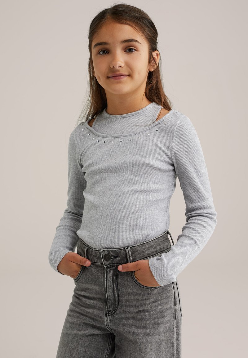 Hellgraues, langärmeliges, geripptes Shirt mit Rundhalsauschnitt, verziert mit kleinen dekorativen Nieten und einem taillierten Schnitt, kombiniert mit hochgeschnittenen grauen Jeans.