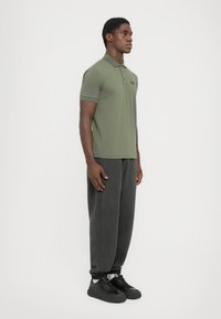 Olive green polo shirt with short sleeves, featuring a collar and logo. Paired with loose, dark gray fleece pants and black sneakers.