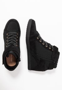 Černé vysoké tenisky s tkaničkami, zlatými očky, bočním zipem a suchým zipem, zobrazené z vrchu a z boku na bílém pozadí.