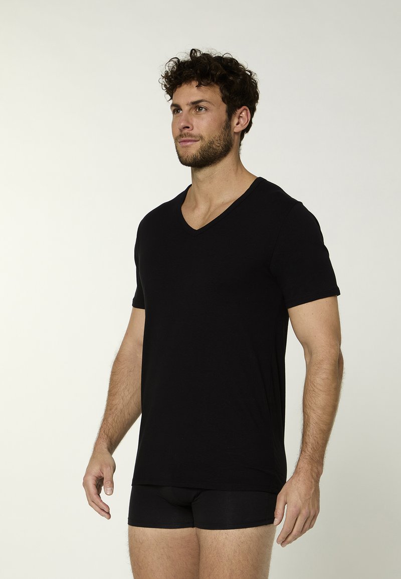 Zwart T-shirt met V-hals van zachte stof, voorzien van korte mouwen en een losse pasvorm. Draagt over zwarte boxershorts, minimalistisch ontwerp.