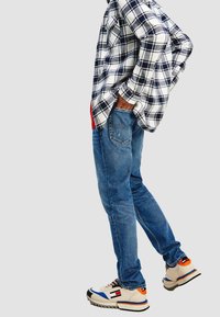 Camicia flanella a quadri bianca e blu navy, t-shirt rossa, jeans blu e sneaker chunky multicolori con suole testurizzate.