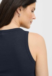 Tirante azul marino de canalé con tirantes anchos, diseño ajustado y textura sutil. El modelo lleva un pendiente de aro plateado en una oreja.