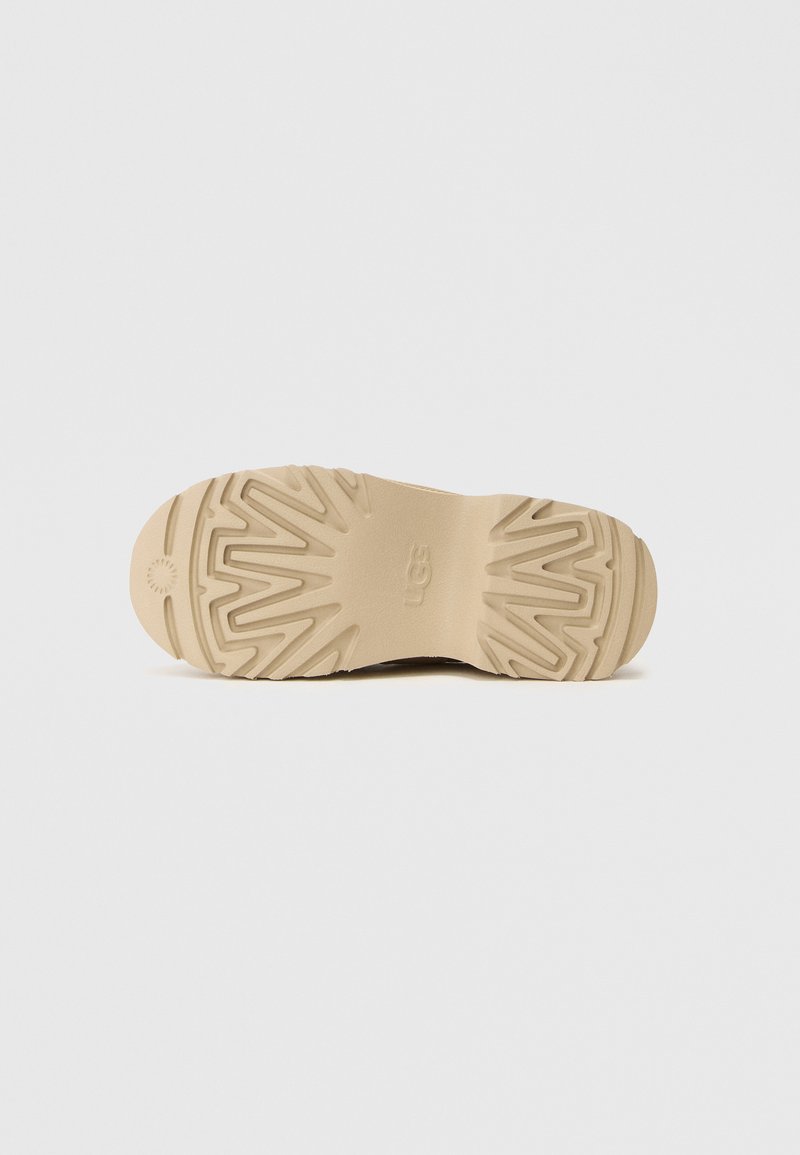 Tan loopzool met een getextureerd grippatroon; heeft een centrale groef en logo op de hiel. Gladmateriaal van duurzaam rubber.