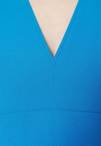 Gros plan sur un vêtement bleu avec un décolleté en V et des coutures visibles le long des bords et de la couture centrale.