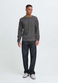 Grå stripete strikkegenser med rund hals, parret med mørkeblå denimjeans. Modellen står avslappet foran en nøytral bakgrunn.
