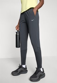 Schwarze Sporthose mit tailliertem Schnitt und strukturiertem Stoff, kombiniert mit schwarzen Turnschuhen und einer schwarzen Wasserflasche.