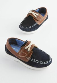 Marineblaue Wildlederschuhe mit braunen Lederakzenten, weißer Naht, elastischem Verschluss und einer texturierten Gummisohle. Innen mit blauer Stoffauskleidung.