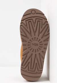 La semelle de la botte UGG est en caoutchouc brun avec un motif de bande de roulement en forme d'étoile et un logo embossé, offrant traction et durabilité.