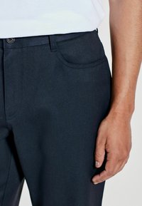 Dark blue trousers made of smooth fabric with a straight cut, featuring a front pocket and waistband with a button closure.