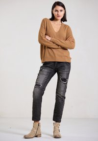 Brown knit sweater with a V-neck, paired with distressed black jeans featuring rips, and beige ankle boots with side zippers.