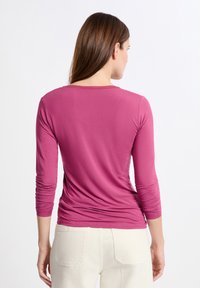Maglietta a maniche lunghe in cotone rosa con scollo rotondo e design aderente, con dettagli arricciati lungo la schiena e le maniche.