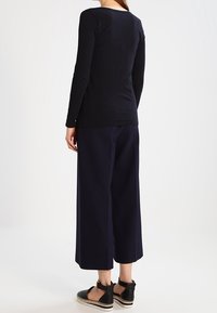 Maglia nera a maniche lunghe con scollatura rotonda, abbinata a pantaloni blu navy a gamba larga e scarpe nere con suola texture e dettagli con cinturino.