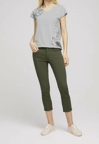 Camiseta de cuello en V a rayas con estampado floral, combinada con jeans recortados de color verde oliva y zapatillas ligeras de color beige. Tela de algodón suave, corte casual.