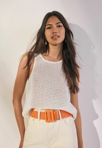 Hvid strikket top med rund halsudskæring, parret med lysfarvede bukser og et lysende orange vævet bælte med en rektangulær spænde.