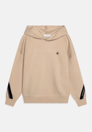 Beige Calvin Klein hættetrøje med sort "cK"-logo på brystet og sort stribe med teksten "Calvin Klein Jeans" på ærmerne.