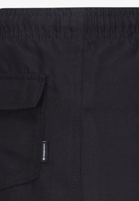 Shorts en tissu noir avec une ceinture élastique, une poche latérale et une petite étiquette de marque cousue sur la couture extérieure.