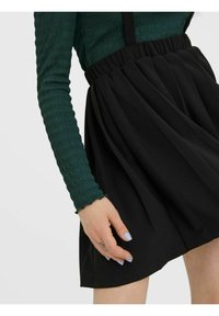 Zwarte rok met een geraffineerde tailleband, gemaakt van een gladde stof. De groene top met lange mouwen heeft een gestructureerd patroon.