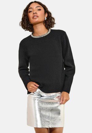 Schwarzer Pullover mit langen Ärmeln und einem Perlenkragen, kombiniert mit einem silbernen metallischen Miniröck mit Krokodilstruktur.