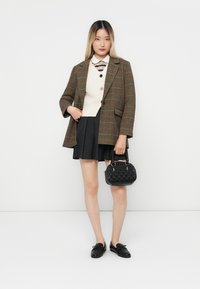 Braun karierter übergroßer Blazer, cremiger Pullover, schwarzer plissierter Rock, schwarze Slipper und eine strukturierten schwarzen Handtasche. Schlichte Kragen Detail.
