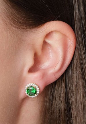 Nahaufnahme eines Ohrs mit rundem Ohrring, der einen großen grünen Edelstein umgeben von kleinen klaren Steinen zeigt.