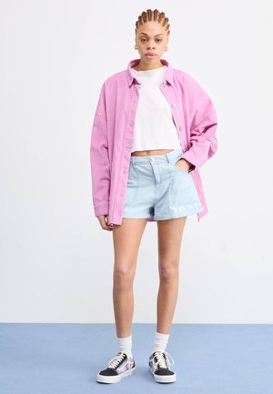 Pink corduroy oversized shirt, white cropped top, light blue shorts, and black sneakers with purple accents. White socks visible.