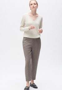 V-ringad krämfärgad tröja, texturerade grå byxor med subtilt rutmönster, och svarta loafers med guldfärgade detaljer.