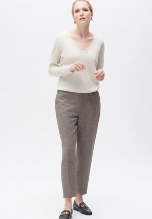 Crèmekleurige V-halstrui, gestreepte grijze broek met een subtiel ruitpatroon, en zwarte loafers met gouden hardware-accenten.