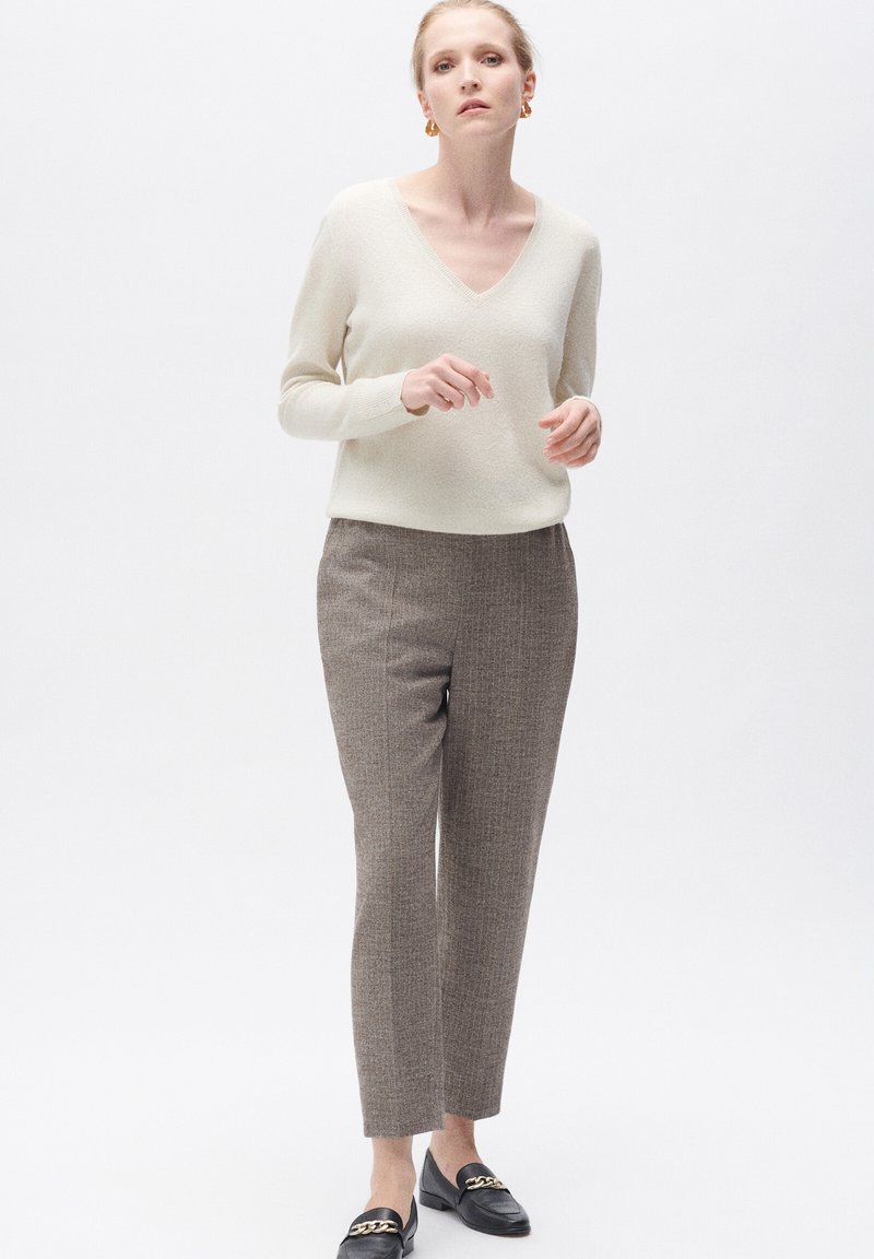 V-ringad krämfärgad tröja, texturerade grå byxor med subtilt rutmönster, och svarta loafers med guldfärgade detaljer.