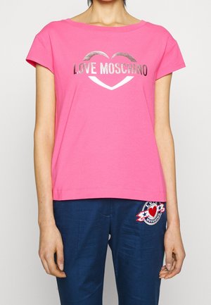 Osoba nosząca jaskraworóżowy t-shirt Love Moschino z metalowym logo oraz granatowe spodnie z naszywką w kształcie serca i gwiazdy.