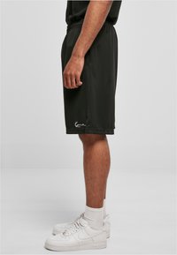 Shorts de sport noirs en matériau léger, dotés d'une taille élastique et d'un détail de logo près de l'ourlet. Portés avec des baskets blanches.