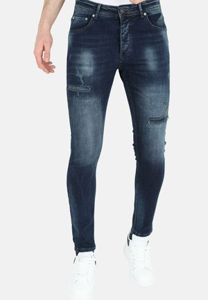 Skinny jeans in donkerblauwe denim met vervaagde plekken en beschadigde patches. Voorzien van steekzakken en een rits. Gepaard met witte sneakers.