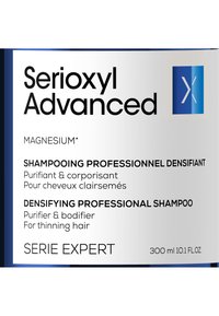 Serioxyl Advanced shampoo fles, 300 ml. Rectangulaire ontwerp, witte en blauwe verpakking, met tekst met productdetails en logo-accenten.