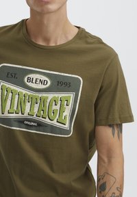 Tamnocrvena pamučna majica s okruglim izrezom i kratkim rukavima, koja sadrži grafički otisak u vintage stilu u bijeloj i zelenoj boji.