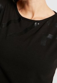 Sort t-shirt lavet af blødt bomuld, med blanke sorte striber på forsiden. Rund halsudskæring og tætsiddende design.