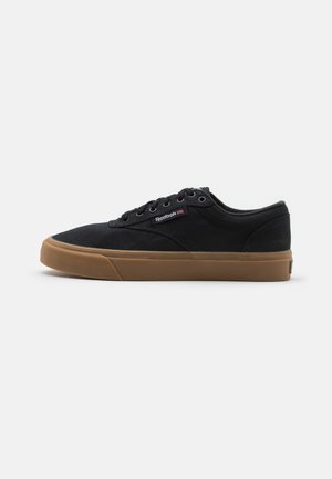 Black canvas sneakers with a low profile, round toe, and brown rubber sole. Features include lace-up design and subtle logo detailing.