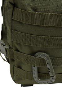 Olive green tactical backpack with textured fabric, multiple attachment straps, and a gray carabiner clip on the side. Durable and functional design.