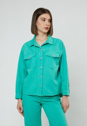 Türkise Denimjacke mit zwei Brusttaschen, Knopfschluss und langen Ärmeln, kombiniert mit passenden Hosen. Glatte Textur und lässiges Design.