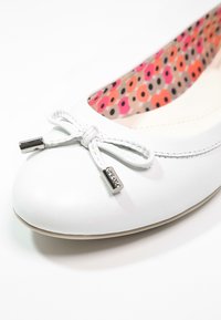 Vit läderballettskor med rund tå, central rosettdetalj, silverfärgade detaljer och ett färgglatt mönstrat inre foder.
