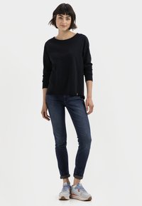 Marineblaue Langarmoberteil, enge Jeans und graue Sneakers mit orangefarbenen Akzenten. Baumwollmaterial, Rundhalsausschnitt und umgeschlagene Säume an den Jeans.