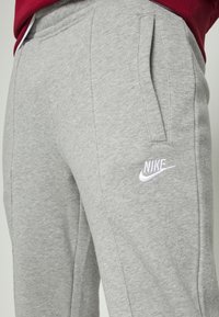 Grå sweatpants gjorda av mjukt material med en slät yta, med sidofickor och en vit broderad Nike-logotyp på vänster sida.