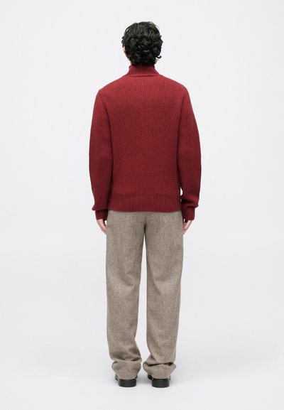 Maroon knit turtleneck sweater with ribbed texture, paired with light brown wide-legged trousers and black footwear.