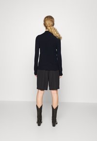 Pull en maille bleu marine associé à un short noir et des bottes chelsea noires de style western, vu de derrière sur fond neutre.