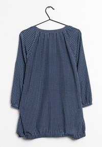 Tunika a maniche lunghe, blu scuro, con motivo a rete con texture, scollatura rotonda e dettagli arricciati sulle spalle, appesa a un gancio nero.