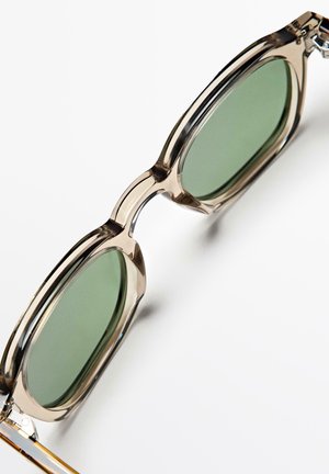 Transparante beige rechthoekige zonnebril met groen getinte glazen tegen een witte achtergrond.